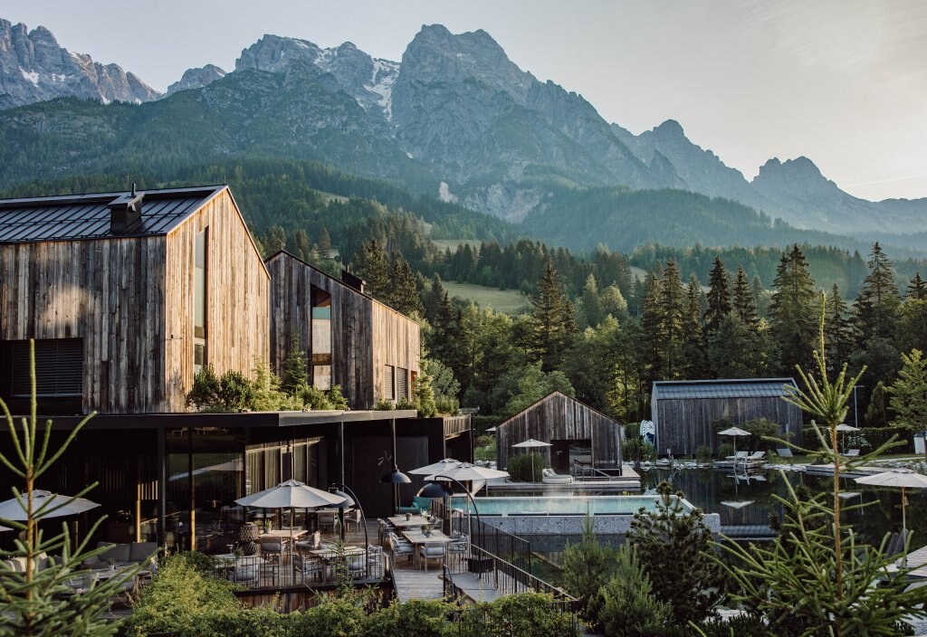 Naturhotel Forsthofgut — the timber houses and bathing lake at dusk