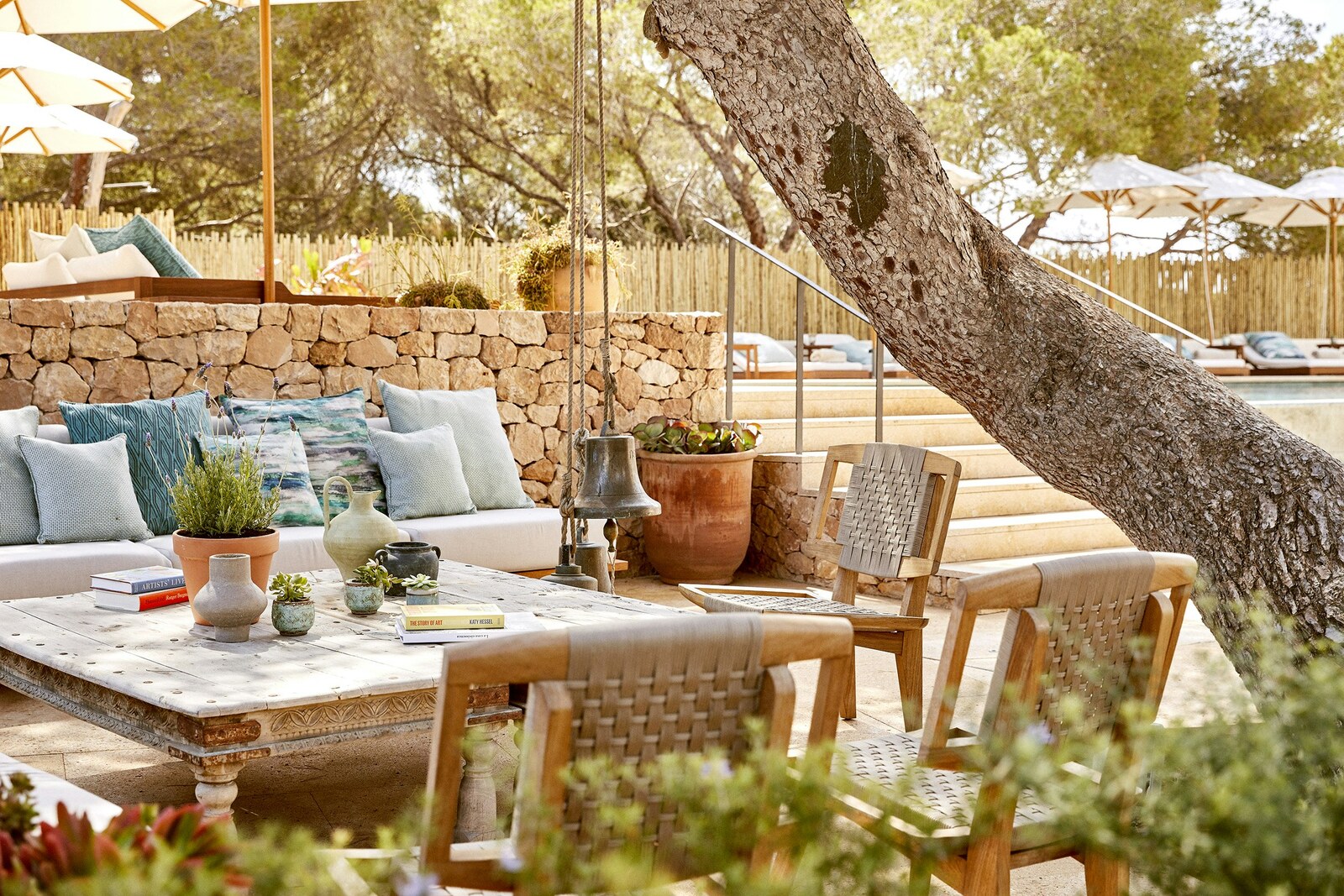 Teranka &mdash; a garden lounge of low sofas around a carved table beneath a pine