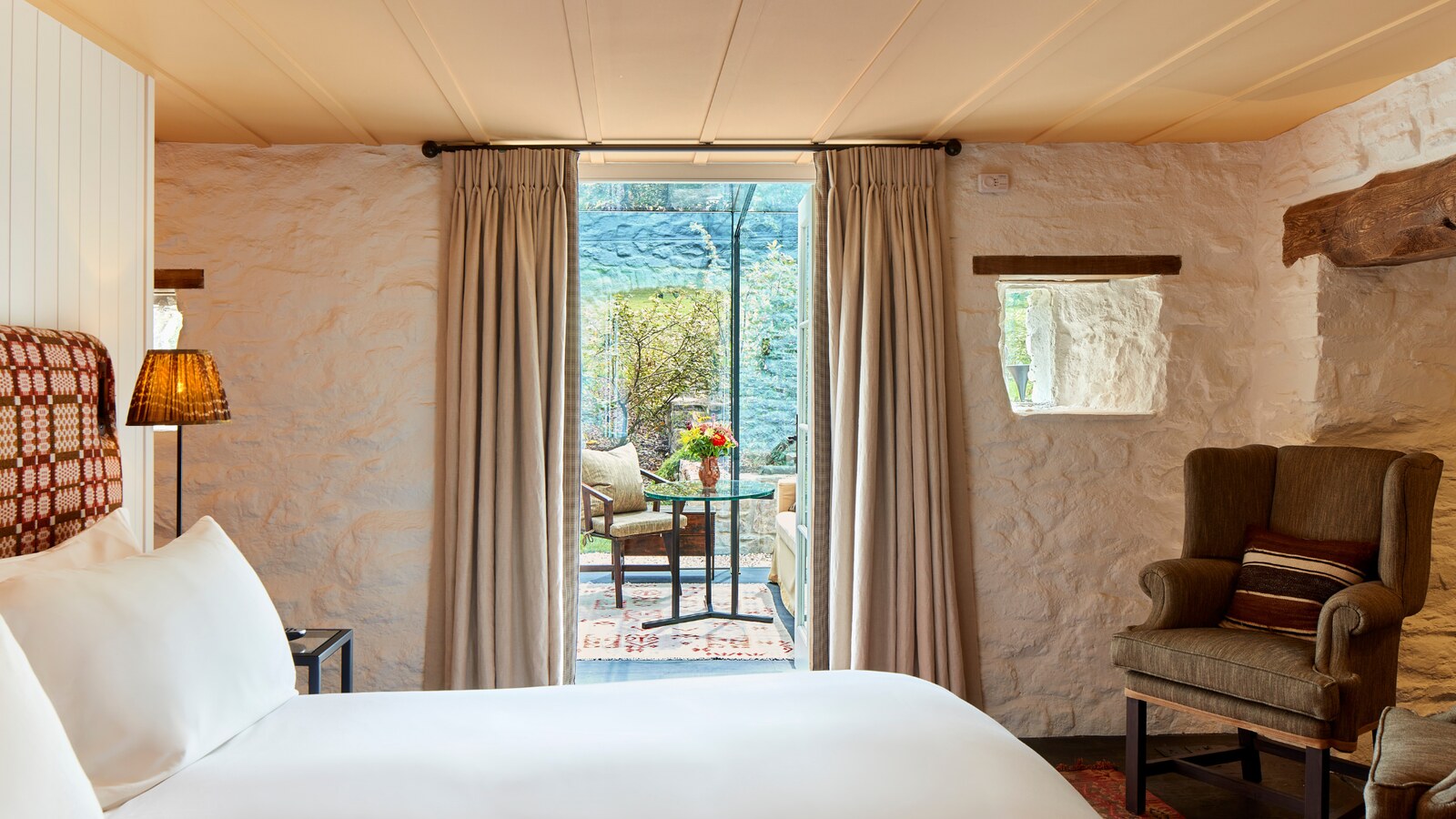 The Grove of Narberth — a cottage bedroom with exposed stone walls opening to the garden