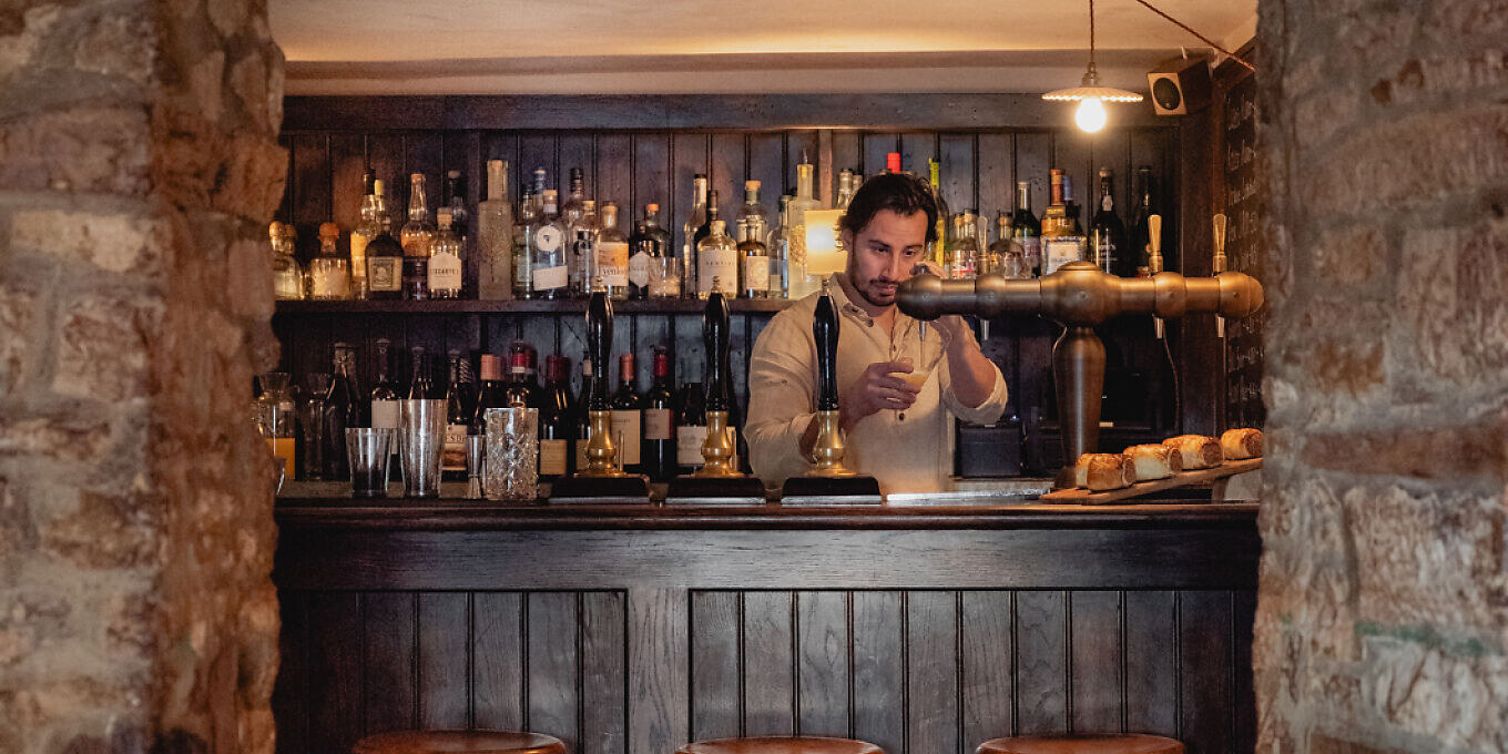 The Bull, Charlbury — the bar, with a bartender mixing a drink against shelves of bottles
