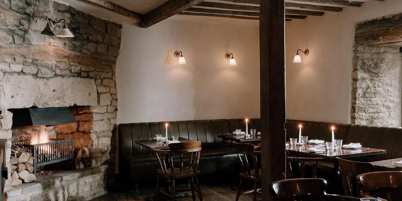 The Bull, Charlbury — the candlelit dining room with a stone fireplace and leather banquette