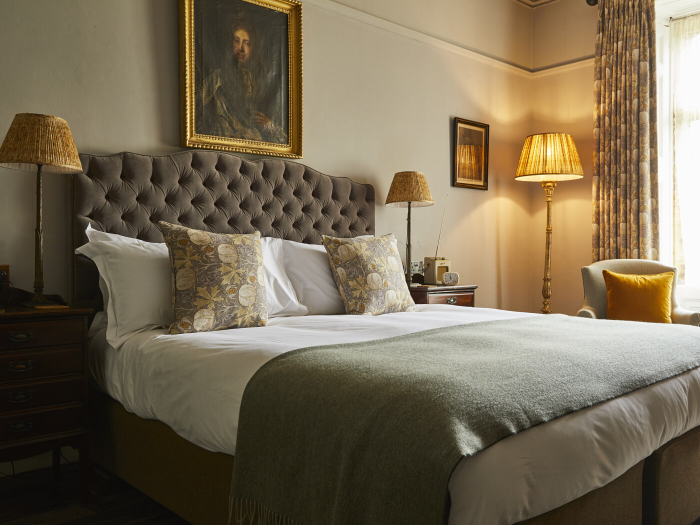 The Pig — a room with a tufted velvet headboard, antique portrait and brass lamps